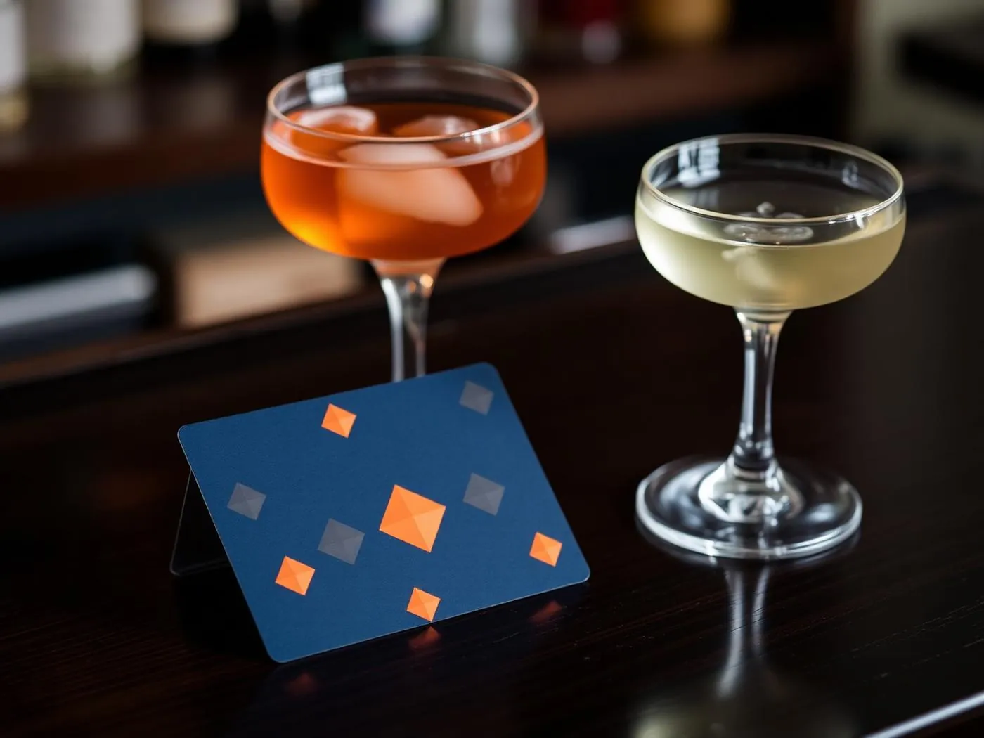 A navy Blue Diamond gift card with orange diamond accents on the bar counter beside two cocktails